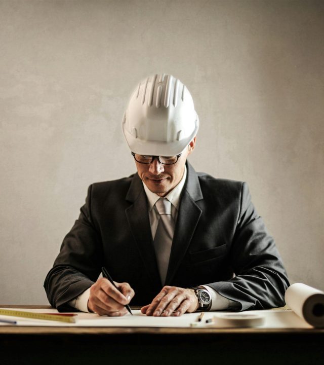 Engineer in a suit drafting architectural plans at a desk indoors.